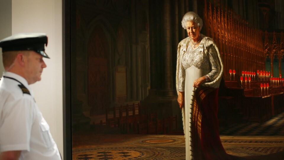 Un gardien de musée fait la garde devant un énorme portrait de la reine.  