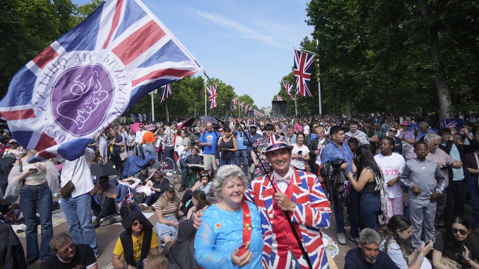 Un homme drapé du drapeau britannique enlace une femme habillée en reine Élisabeth II dans une foule à Londres.