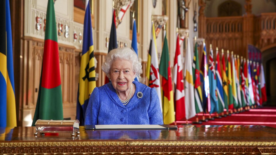 La reine, assise à un bureau devant les nombreux drapeaux des pays faisant partie du Commonwealth.