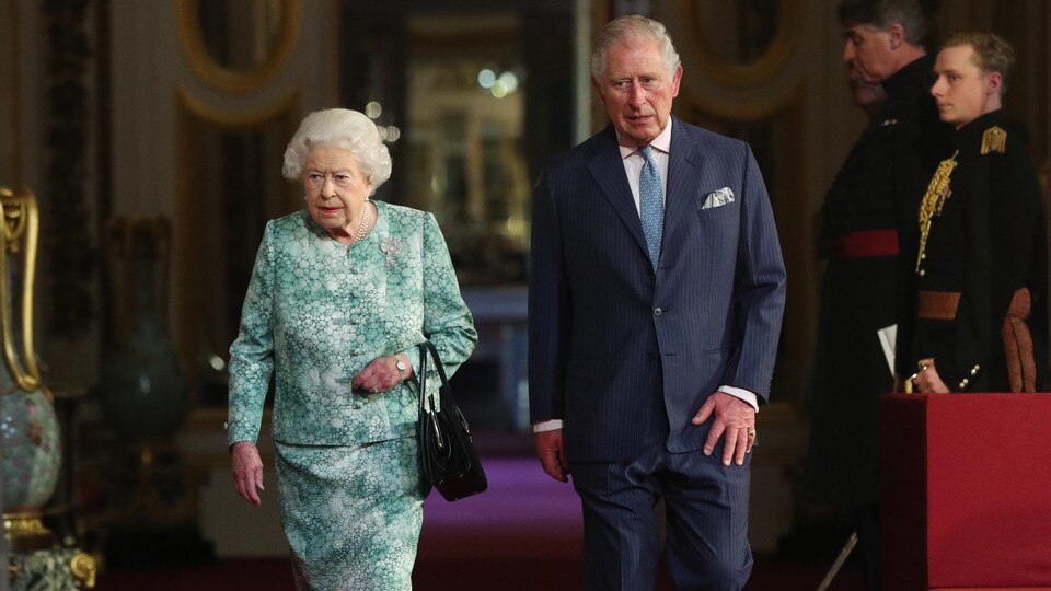 Élisabeth II et le prince de Galles marchent côte à côte sur le tapis rouge du palais de Buckingham.