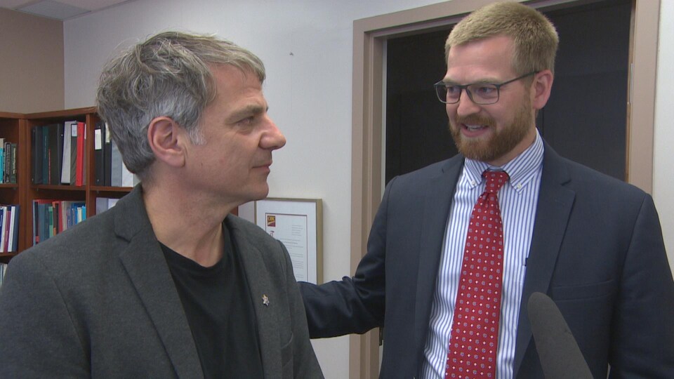 Deux hommes en veston se regardent intensément avec émotion dans un bureau.