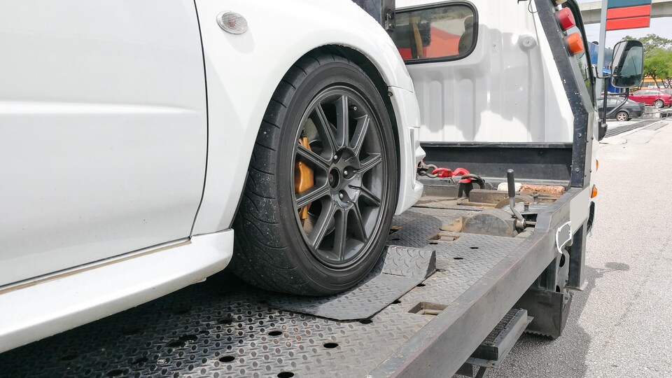 Une voiture est transportée par une remorqueuse.