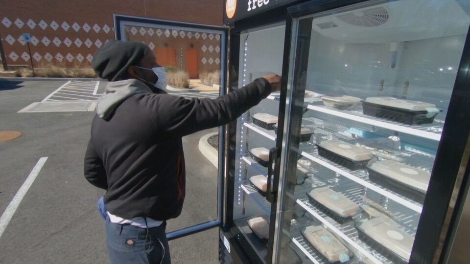 Un homme choisit un repas dans un réfrigérateur à l'extérieur.