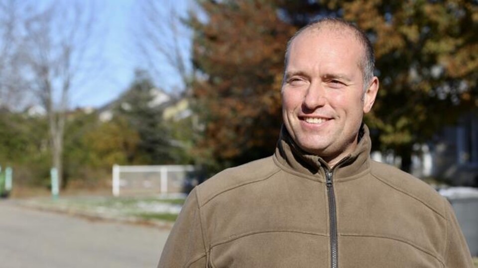 Un homme souriant devant un décor d'automne