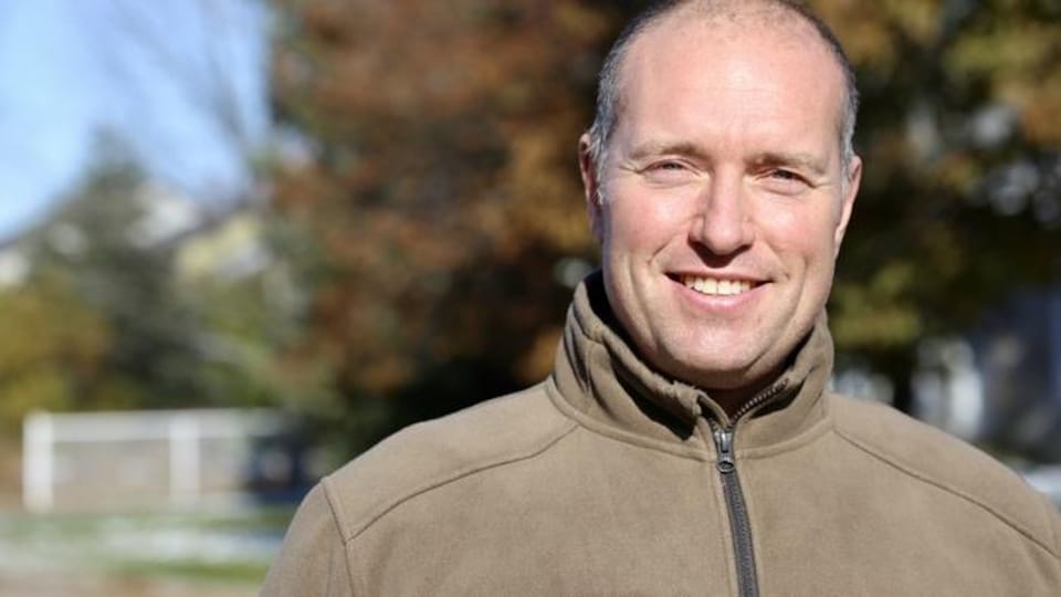 Un homme souriant devant un arbre jauni par l'automne