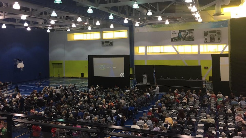 Des centaines de personnes assises dans un gymnase.
