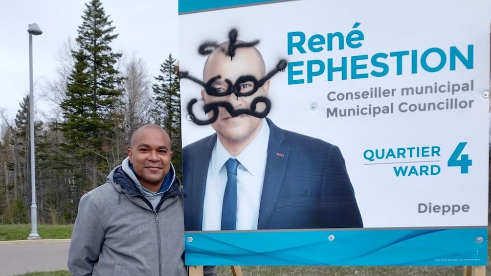 Le candidat René Ephestion à côté d'une affiche életorale.