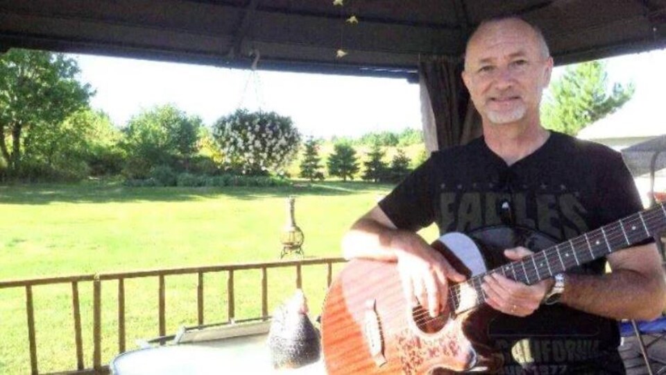 Un homme souriant sur un patio, une guitare entre les mains.