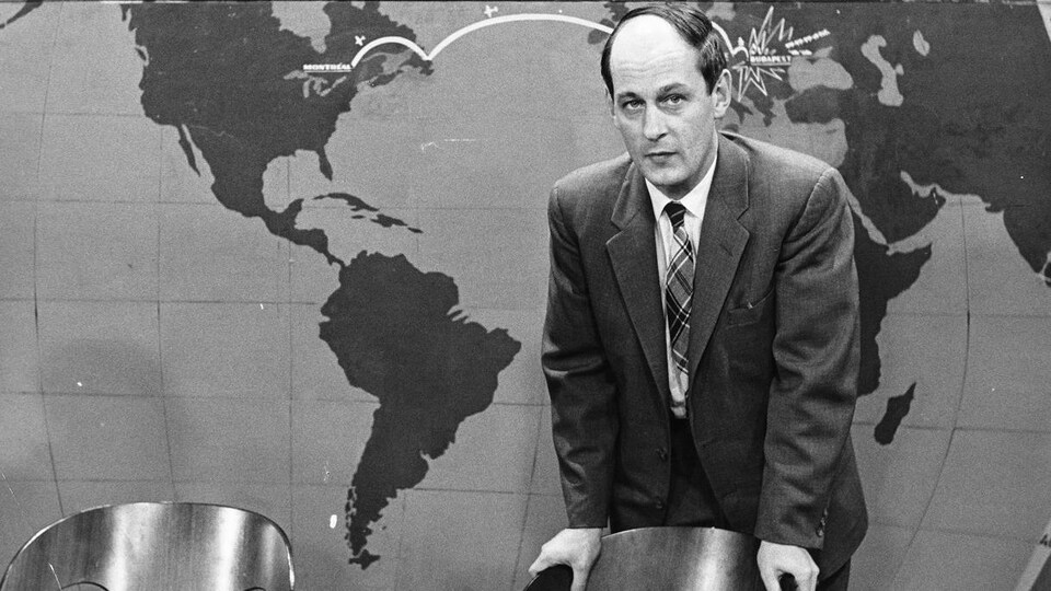 Standing in front of a world map, host René Lévesque is leaning back in a chair, a cigarette between his fingers.