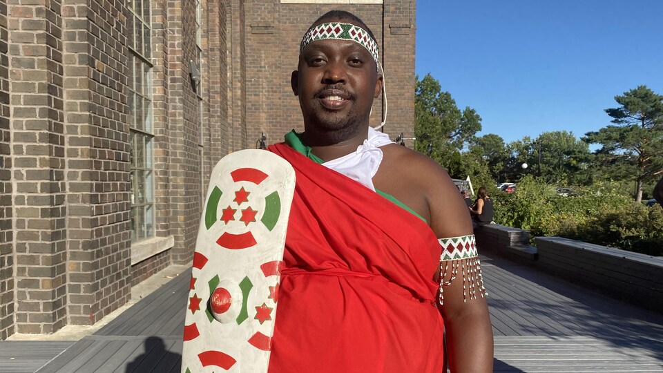 Renord Nsekera devant un tambour avec un bouclier à l'effigie du drapeau burundais.