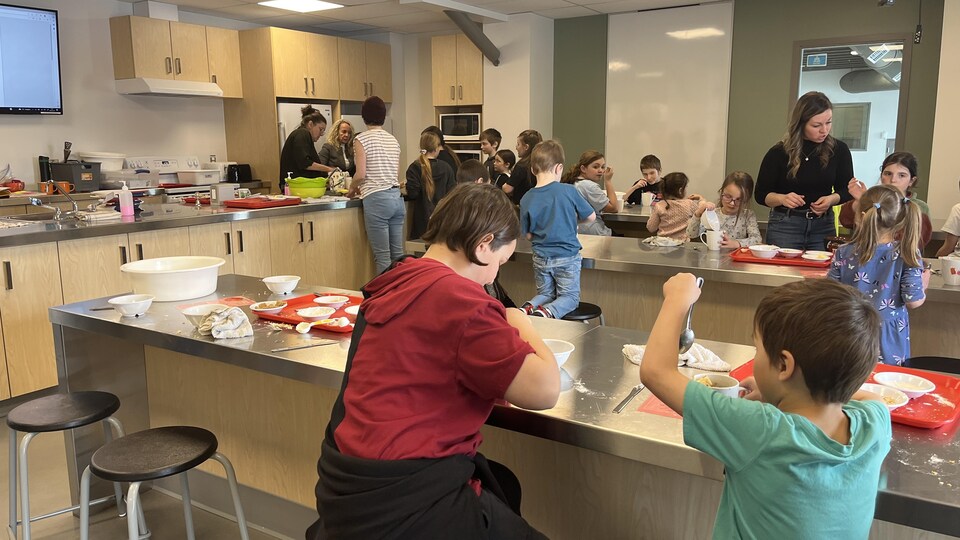 Une cuisine avec des enfants qui cuisinent sur des tables accompagnés de professeures.