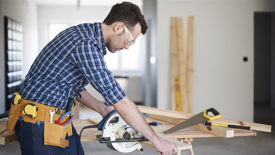 Un homme coupe une planche de bois.