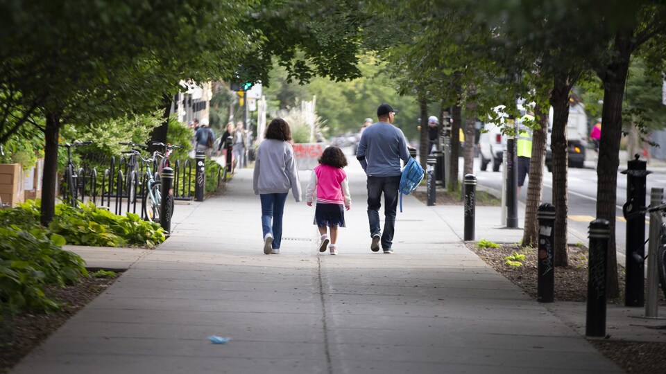Des parents avec leur fille sur le trottoir couvert d'arbres feuillus.