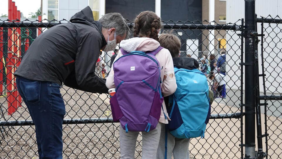 Un père portant un masque et ses deux jeunes enfants arrivent à l'école.