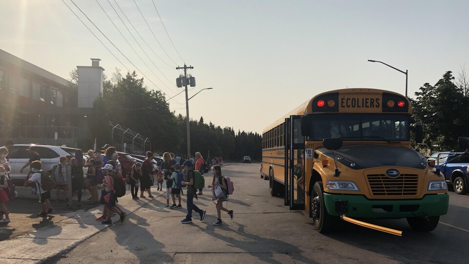 De jeunes élèves qui sortent d'un autobus scolaire avec leur sac d'école sur le dos.