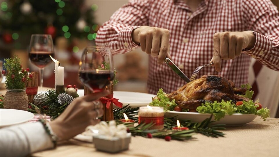 Un homme coupe une dinde autour d'une table décorée pour Noël.