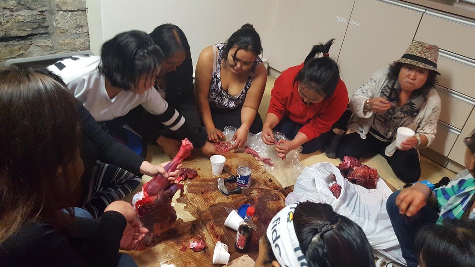 Des femmes inuit mangent, assises par terre, de la viande de caribou décongelée et crue.