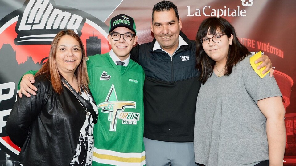 Paul Vollant entourent ses proches de ses bras devant une affiche de la LHJMQ, au Centre Vidéotron, à la suite de l'annonce du repêchage de son fils.