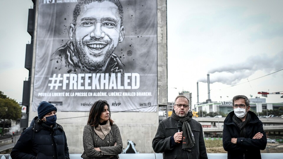 Deux femmes et deux hommes debout devant une immense affiche représentant un homme souriant avec l'inscription FreeKhaled