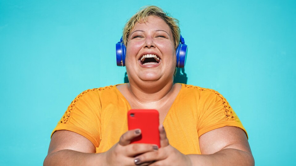 Une femme écoute du contenu sur son téléphone cellulaire à l'aide de ses écouteurs sans fil.