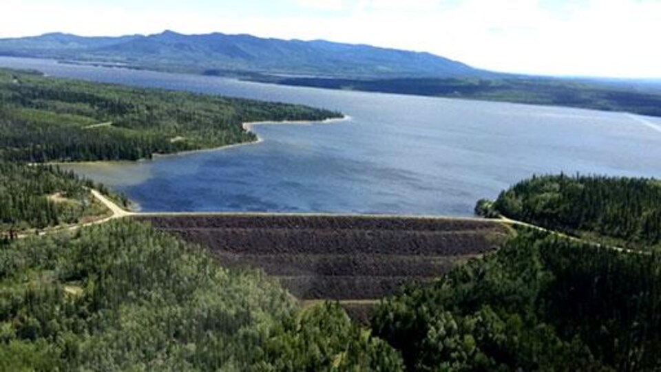Des forêts et un lac, avec un barrage au centre, des montagnes en arrière-plan.