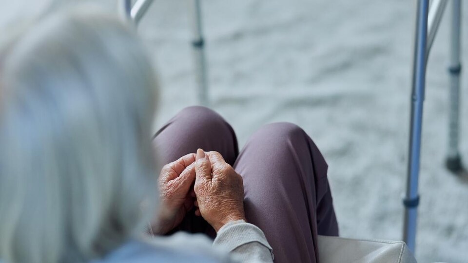 Une femme âgée assise à côté de son déambulateur.