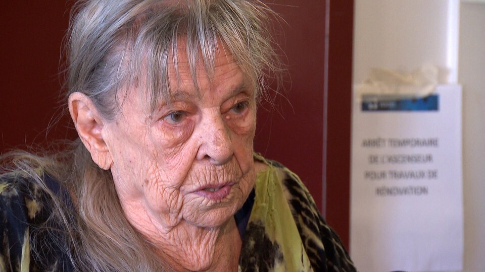  Louisette Simard-Paquette, 92 ans. Elle est devant un ascenseur avec une affiche d'arrêt temporaire. 