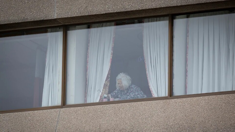 Une personne âgée résidant dans une maison de soins de longue durée à Toronto photographiée à travers une fenêtre.