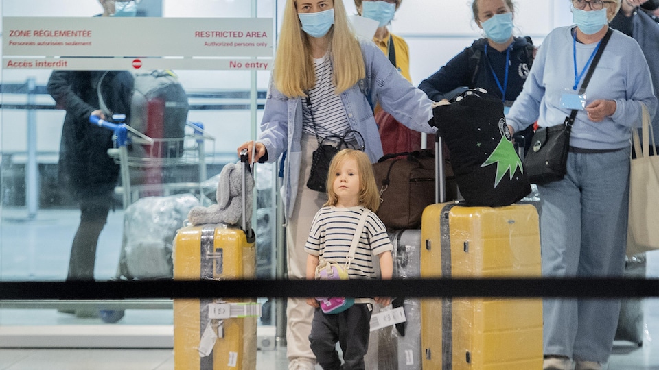 Des ressortissants ukrainiens, dont une femme et un enfant, qui fuient la guerre en Ukraine arrivent à l’aéroport Trudeau de Montréal avec leurs valises jaunes.
