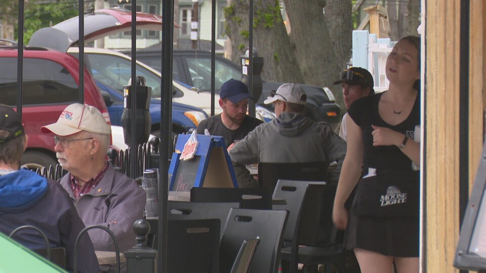 Des clients mangent sur une terrasse. Une serveuse s'approche d'une table pour vérifier que leur repas se déroule bien.