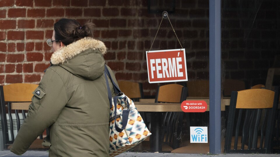 Une femme passe devant la façade d'un restaurant où une pancarte indique qu'il est fermé.