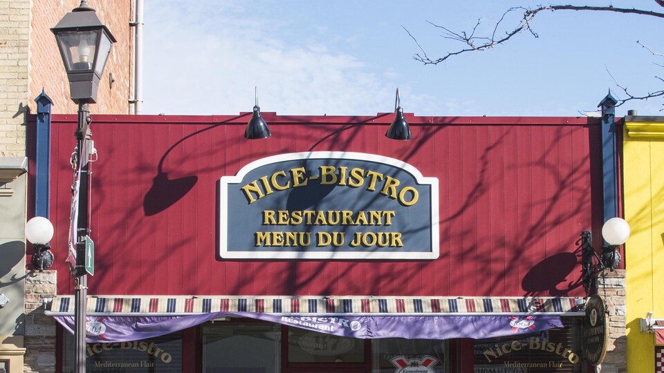 Vue de la façade principale du restaurant Nice Bistro avec l'enseigne et les lumières extérieurs, en plein jour.
