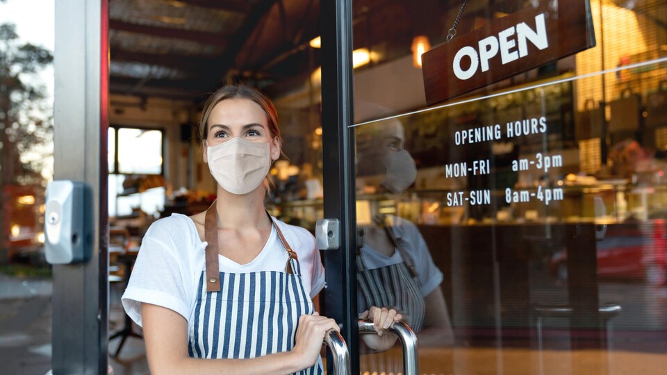 Une femme portant un masque ouvre la porte d'un café.