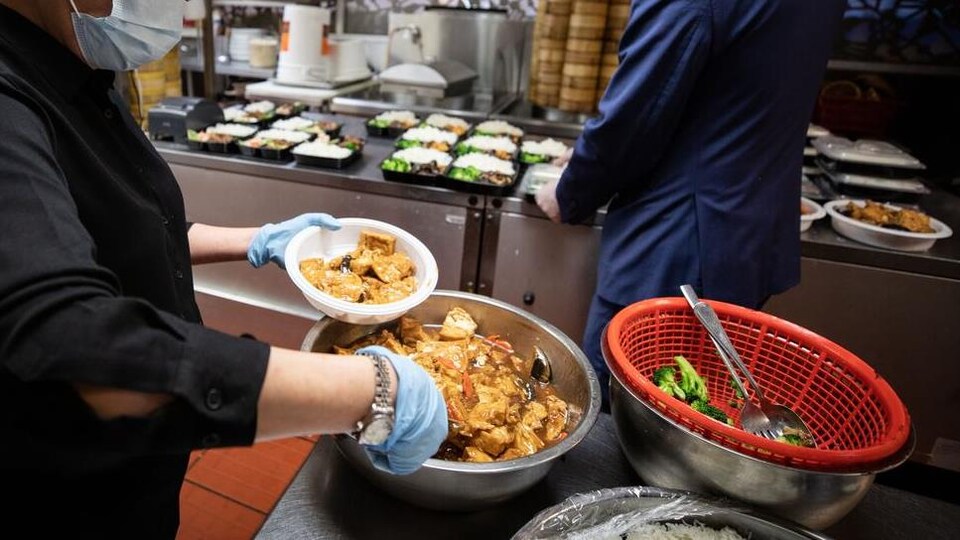 Des cuisiniers portant des masques préparent des plats pour emporter.
