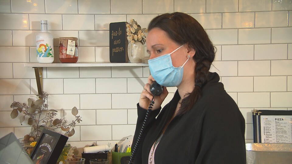 La propriétaire du restaurant Pizzeria NO. 900 de Sherbrooke, Claudia Pelletier en train de prendre une commande téléphonique derrière un comptoir.