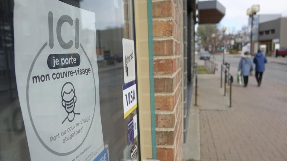 Une affiche dans la porte d'un commerce rappelle le port du masque obligatoire.