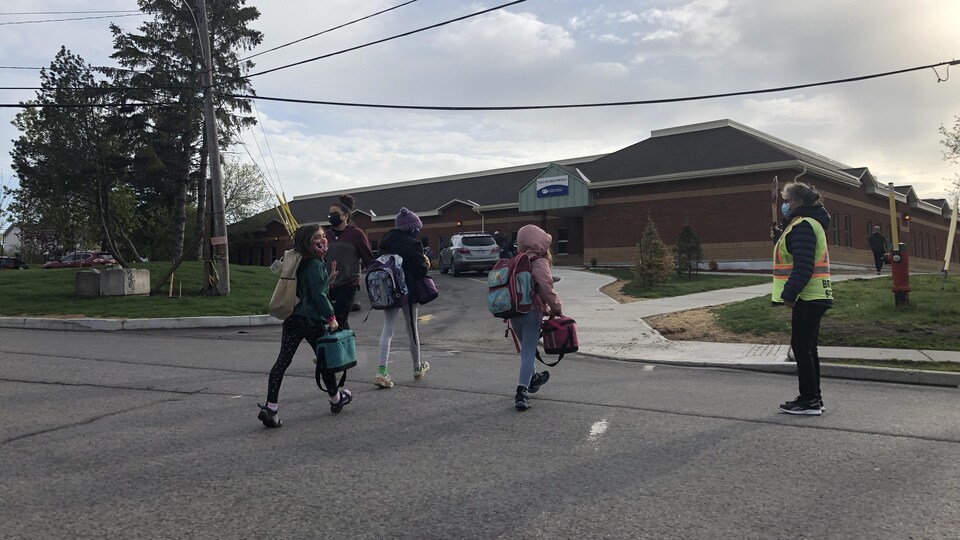 Des élèves arrivent à l'entrée d'une école, une brigadière assure la circulation.