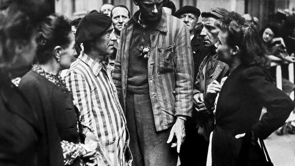Des femmes entourent des hommes vêtus des vestes rayées des prisonniers des camps nazis.