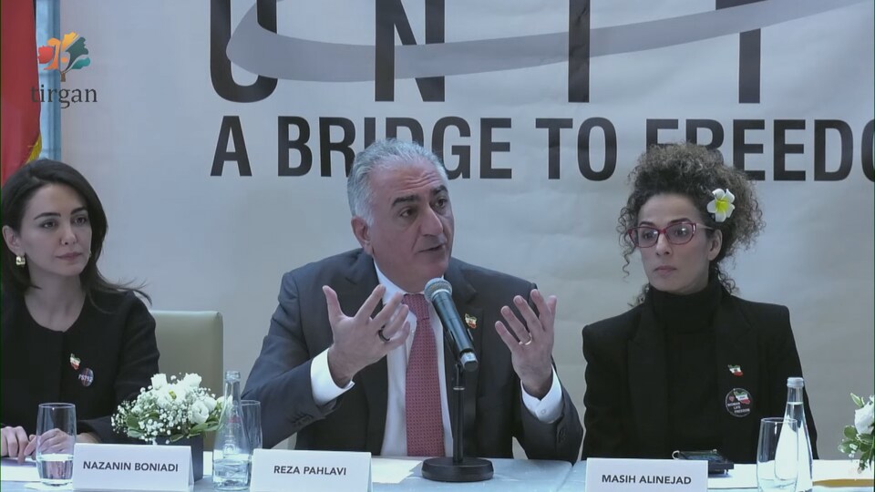 Reza Pahlavi, assis, est en train de parler au micro.