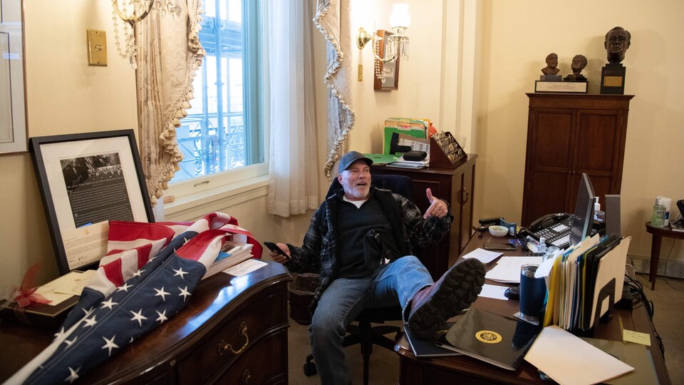L'homme a un pied posé sur le bureau de madame Pelosi.
