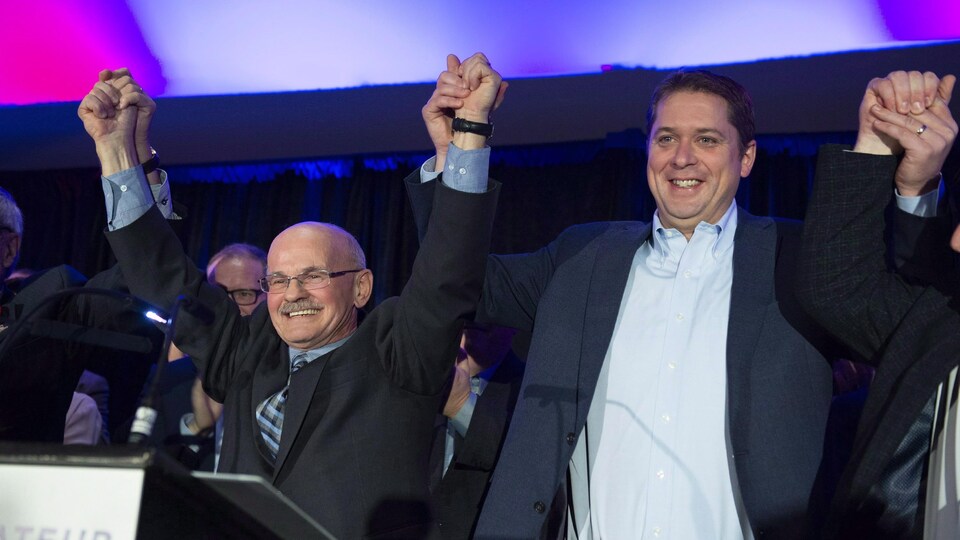 Richard Lehoux et Andrew Scheer, sourient en se tenant la main, les bras dans les airs.