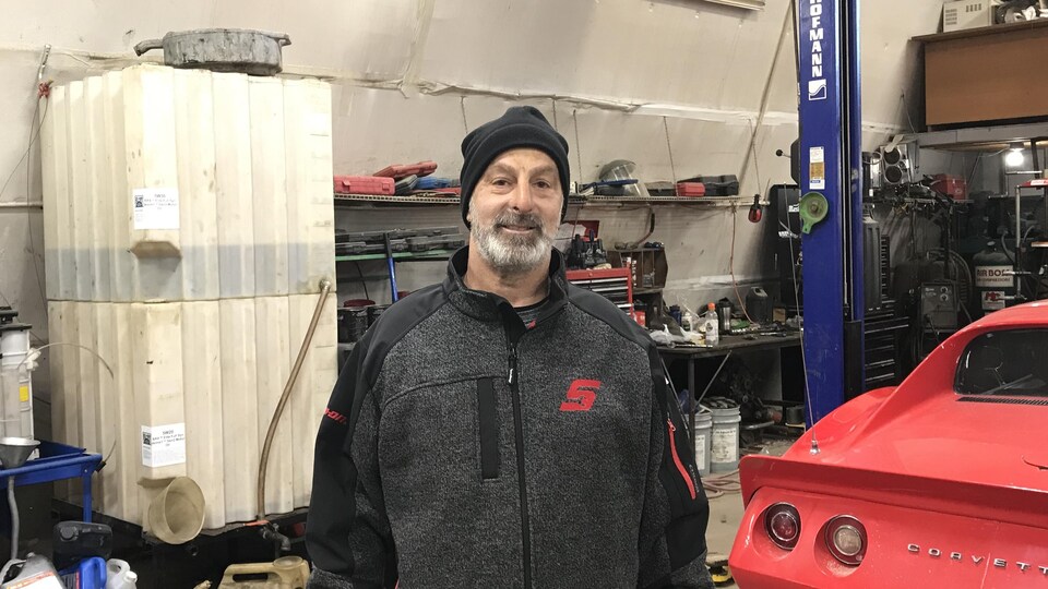 Richard Pelletier photographié dans son garage, derrière une voiture rouge. 