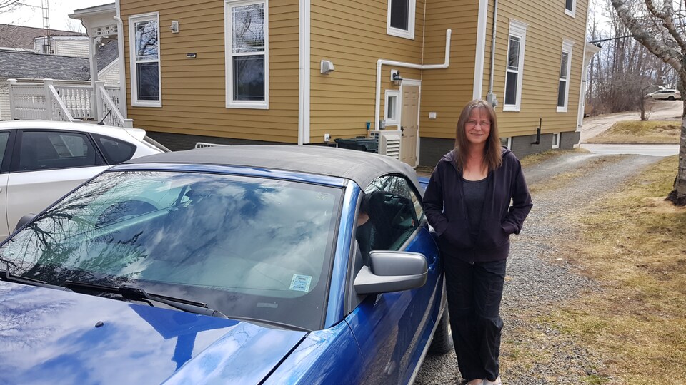 Rebecca Richardson debout, souriante, à côté de sa voiture, devant sa maison.