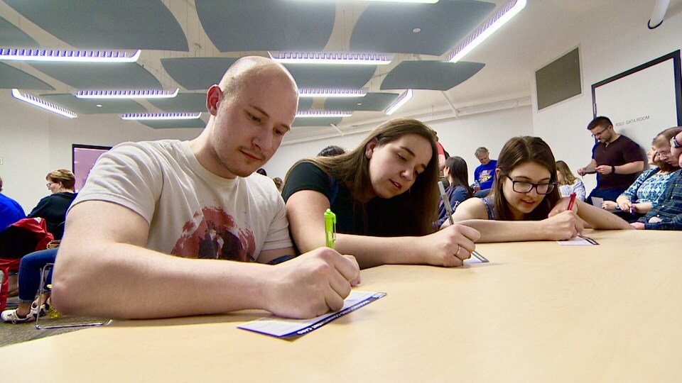 Trois étudiants signent des cartes de membres sur une table beige. 