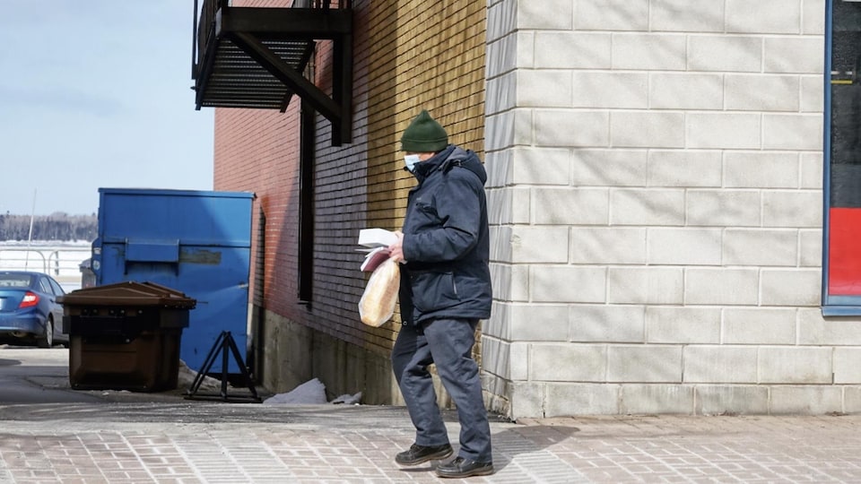 Une personne qui porte un masque marche sur le trottoir.