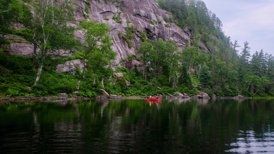 Un canot sur une rivière à côté d'une haute falaise rocheuse.
