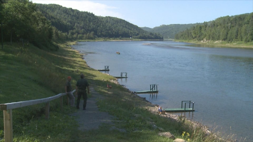 Deux homes regardent la rivière Restigouche bordée de quais.