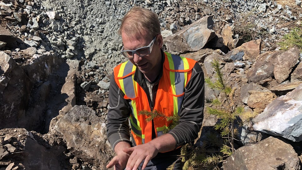 Un homme observe un site minier abandonné. Il porte des lunettes de sécurité et un dossard.