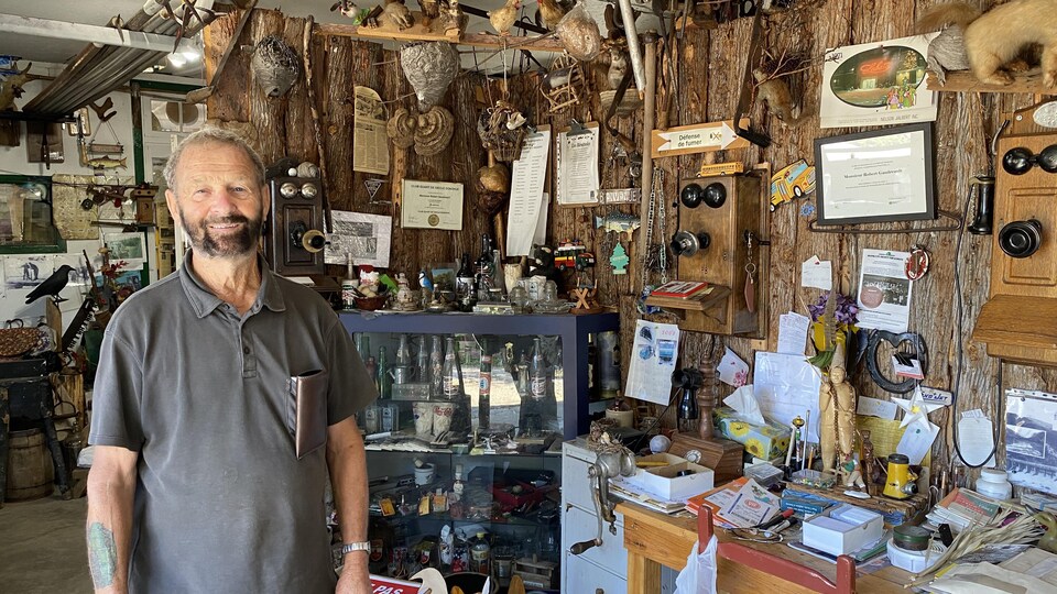 Un homme âgé sourit à la caméra devant des objets antiques liés à la drave. 