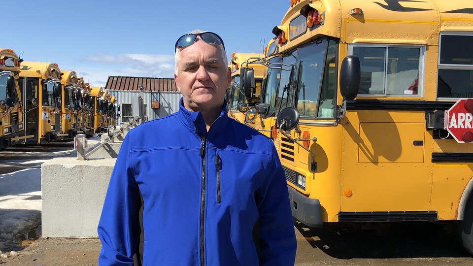 Le président du syndicat des chauffeurs scolaires d'autobus Manic, Robert Jean, pose devant deux rangés d'autobus.